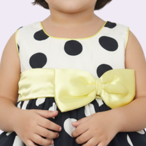 Detalle frontal del vestido de niña lunares negro y blanco con moño amarillo removible